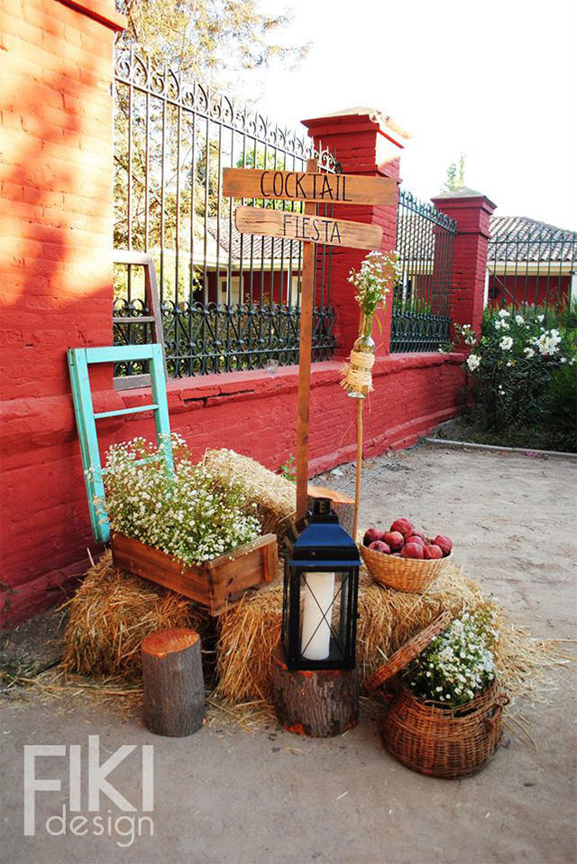 Decoración en una casa con fardos de paja, cajón y canastas con flores y frutas, tronquitos y sobre uno de ellos un farol.