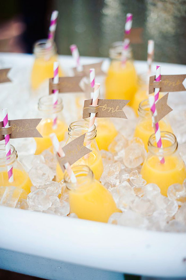 Cooler lleno de cubitos de hielo con botellas de vidrio, bombilla incluída, de jugo de naranja