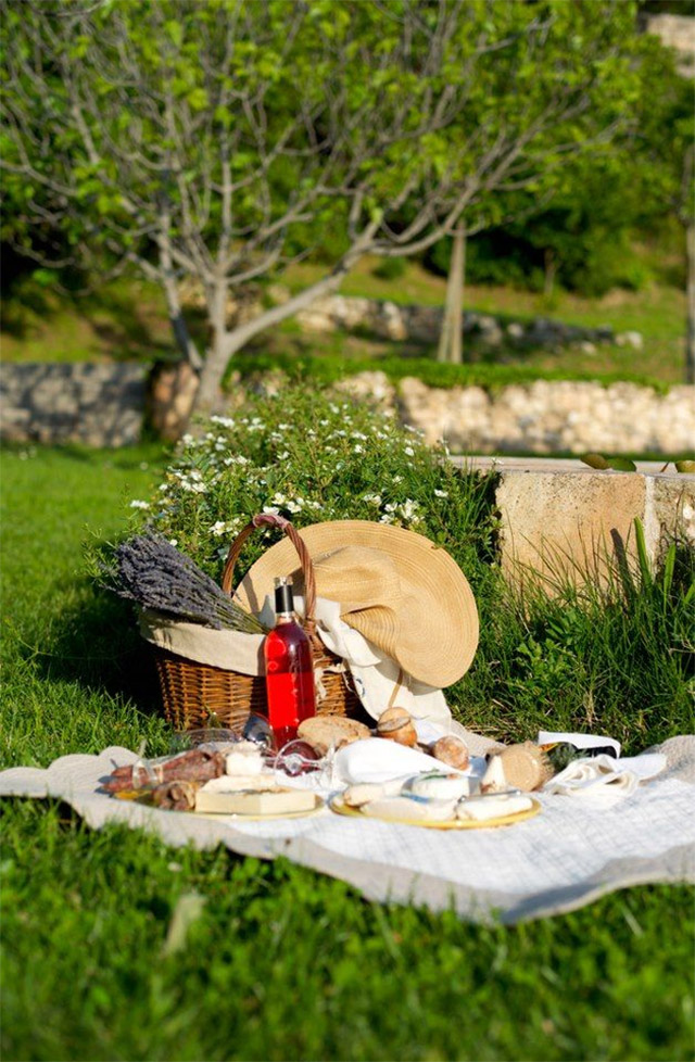 Picnic en el parque, mantel blanco, quesos y embutidos, copas, botella de vino y la canasta de mimbre donde llevar todo lo necesario para el picnic.