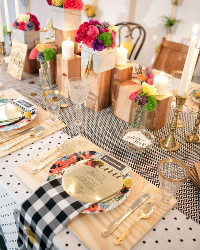 Mesa decorada con elementos de madera como los individuales y algunos cubos donde se ubicaron pequeños arreglos florales y algunas velas.