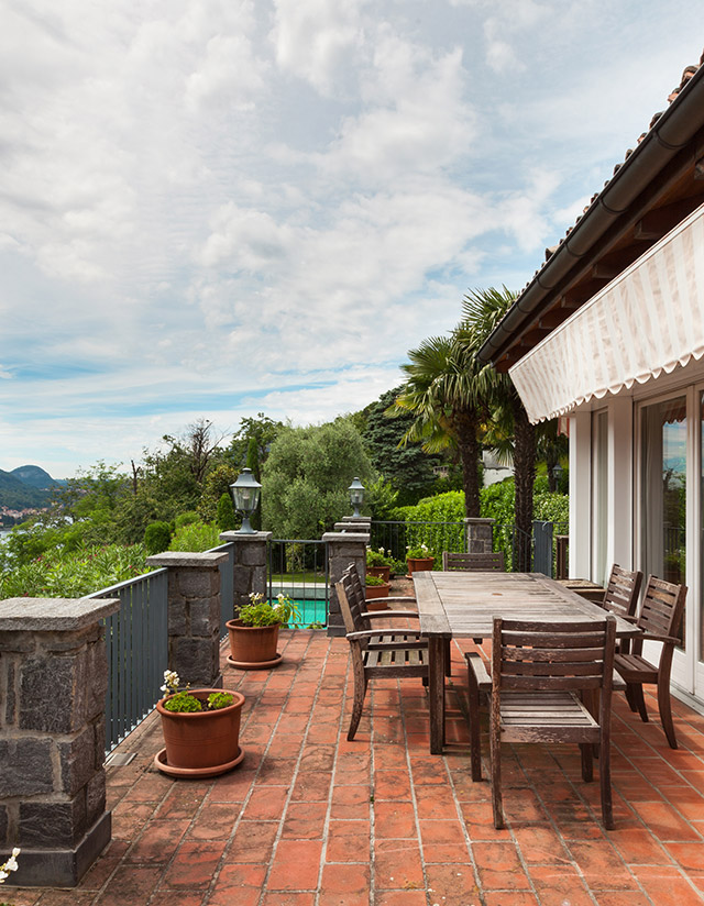 Terraza de casa con vista al jardín, juego de comedor de madera, toldo de lona.