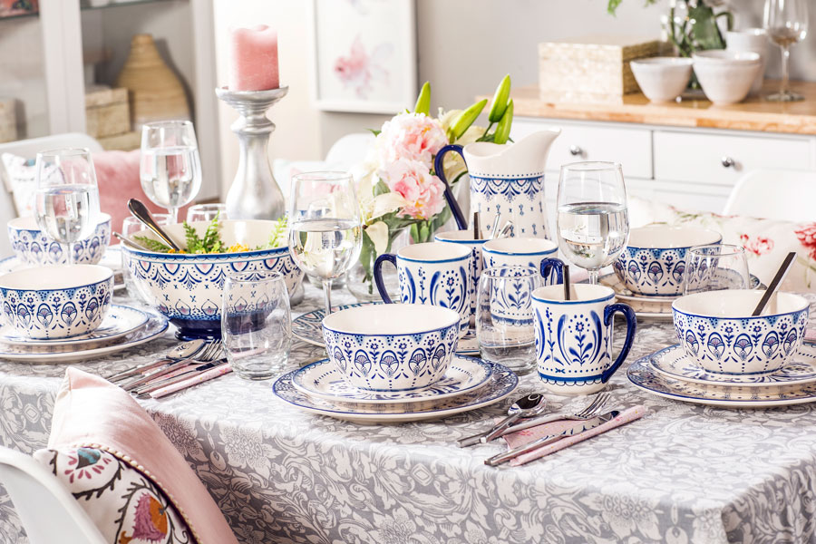 Fotografía de mesa de comedor con vajilla puesta. Vajilla es de color blanco y tiene diseños color azul y celeste por el exterior.