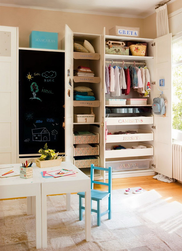 Habitación infantil femenina con una mesita, silla calipso, ropero abierto con cajones etiquetados y un muro pizarrón al costado del ropero.