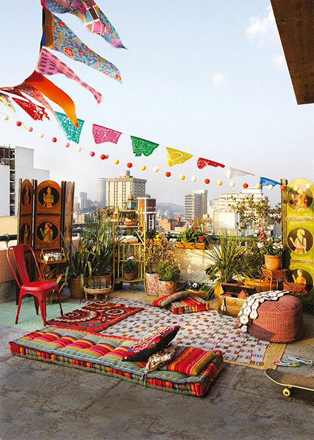 Terraza con cojines y textiles estilo hindú en tonos rojos y decoración aérea multicolor