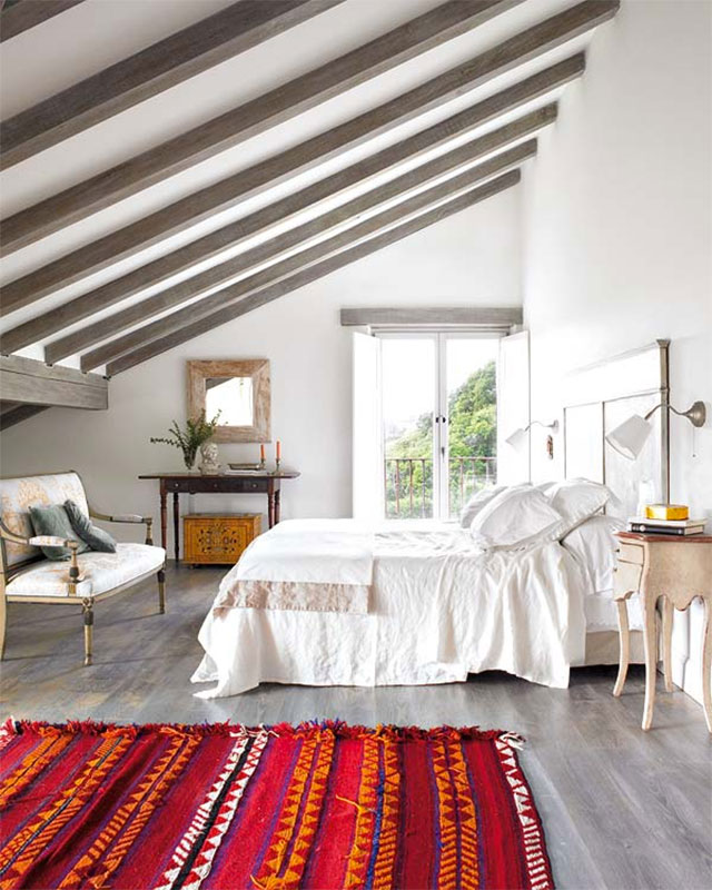 Cama con cubrecama blanco, dormitorio con piso laminado y alfombra roja con diseño de grecas