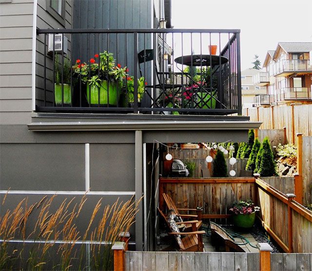 Vista de un balcón en un segundo piso y una terraza en el primero. El balcón con un juego de terraza de tres piezas y maceteros color verde manzana con plantas y flores.