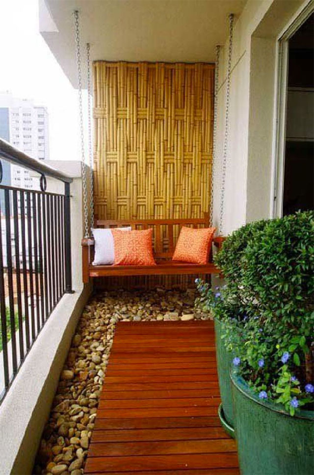 Balcón con un muro de madera de bambú, piso con piedras y un caminito con decking de madera. Sujeto desde el techo con cadenas y apegado al muro de bambú un sillón de madera.