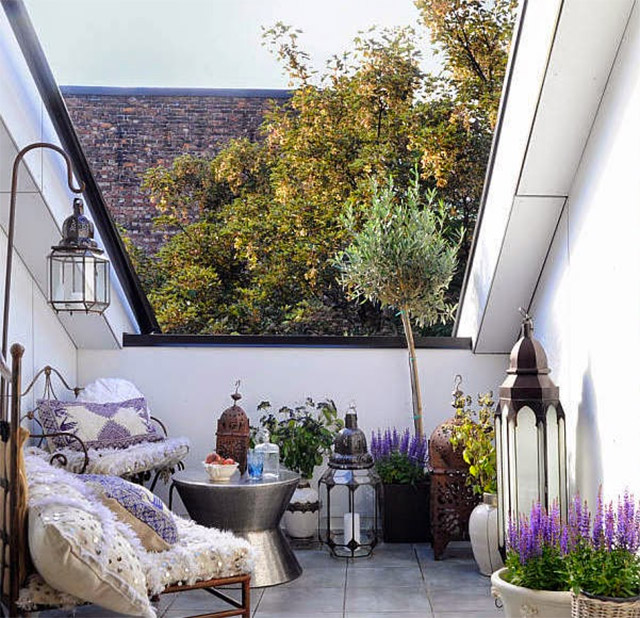 Terraza con un par de sillones, decorada con muchas plantas, una mesa de centro plateada y faroles grandes.