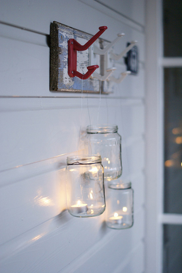 Frascos de vidrio con velas tea light en el interior colgados desde un perchero.