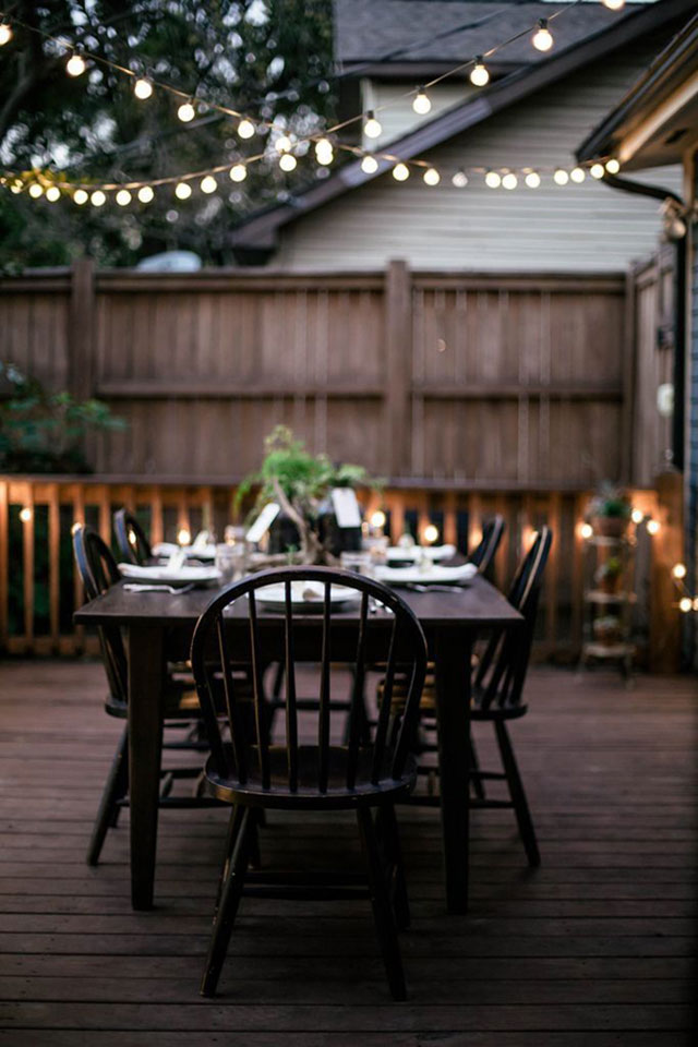 Comedor de madera en la terraza iluminado con guirnalda de luces.