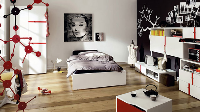 Dormitorio con una pared blanca y la otra negra con sticker blanco de árbol. Cama, velador, ropero, rack TV y estante de madera lacada blanca y detalles en rojo de líneas simples. Ropa de cama en negro y gris, busto de maniquí blanco con collares.