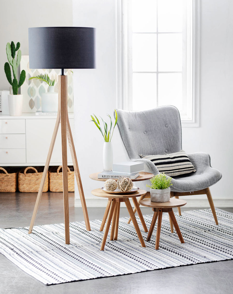 Imagen de living o sala de estar con luz exterior, muebles estilo minimalista, una poltrona color gris, mesas auxiliares de madera y una lámpara con patas de madera y pantalla negra