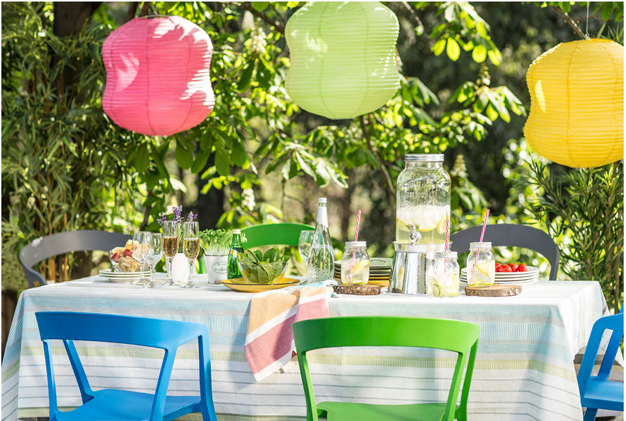 Mesa exterior con mantel a rayas, lámparas de papel de colores y la mesa lista para un almuerzo al aire libre