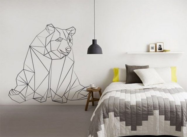 Pared blanca de dormitorio con el dibujo geométrico de un oso sentado.