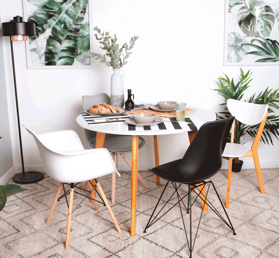 Comedor blanco con cuadros y láminas con plantas, sillas en blanco, negro y gris.