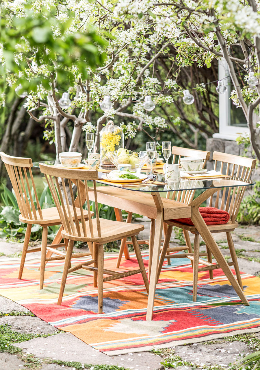 Terraza con alfombra sobre la cual hay una mesa de comedor con sillas de madera en juego, y superficie de mesa es de vidrio, para un diseño