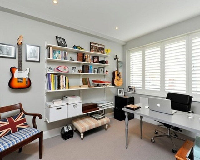 espacio de trabajo con onda rockera, con guitarras colgadas de la pared. Escritorio de mesa gris y patas torneadas. La luz proviene de un ventanal detrás del escritorio, regulable la luz a través de persianas.