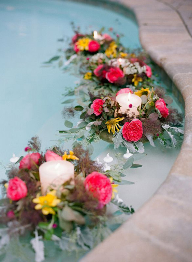 Borde de piscina con arreglos florales y una vela al centro del arreglo.