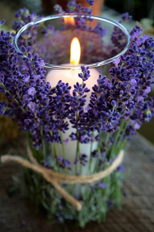 Porta vela de vidrio con el resto de una vela dentro. Por fuera unas ramitas de lavanda amarradas con un cordel.