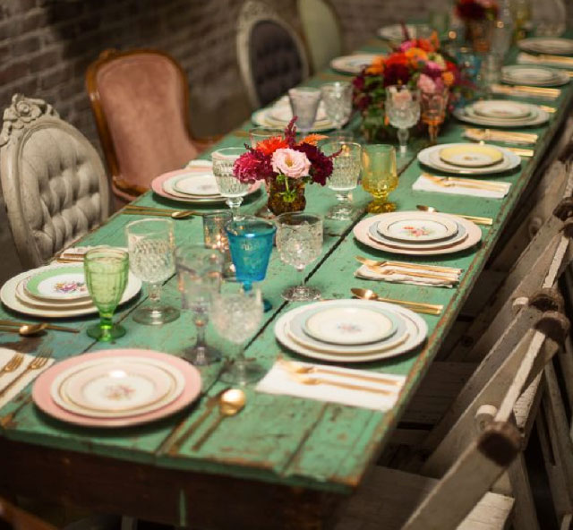 Mesa de comedor estilo rústico de madera pintada verde. Menaje de distintos colores y sillas diferentes.