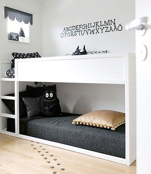 Dormitorio infantil con un camarote, decorado en blanco y negro. Cortina negra con puntitos blancos, cama superior con cojines y cubrecama negro y puntos blancos, cama inferior con cojines y cubrecama negros y un cojín dorado.