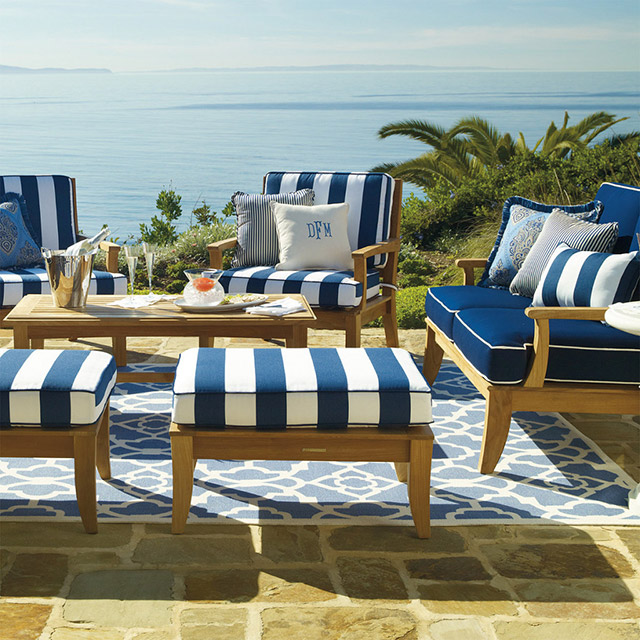 Juego de living de terraza estilo marino con vista a la playa. Alfombra celeste con patrón lineal de flores blancas y borde blanco.