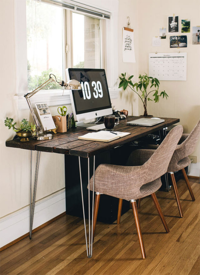 Espacio de trabajo de look totalmente natural con elementos como la madera, en la cubierta del escritorio, y macetas con plantas, que se pueden ver sobre el escritorio y a un costado. Todo frente a la ventana, que da la luz natural perfecta para trabajar.