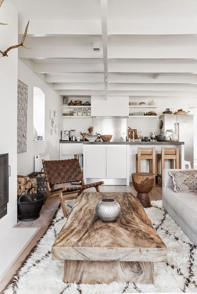 Sala de estar con una gran mesa de centro de madera, con un estilo bastante rústico que podemos ver en el piso, a un costado del sillón y en los taburetes de madera en la cocina.