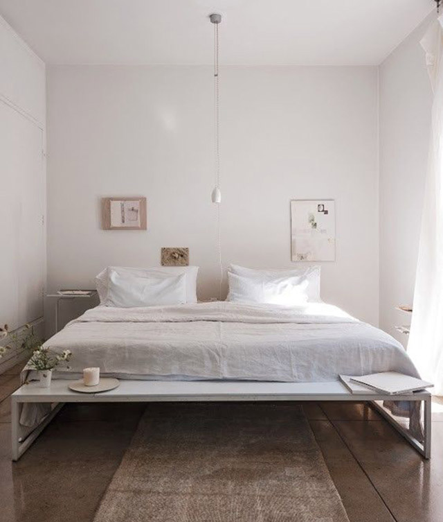 Base de cama de madera blanca más grande que el colchón para dejar una banqueta a los pies de la cama.