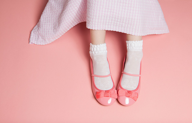 Pies de niña con vestido rosado, calcentines blancos y zapatos de charol rosado.