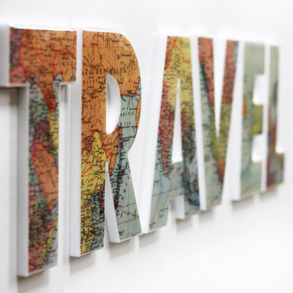 Letras pegadas a la pared que dicen TRAVEL. Estan en relieve hechas con mapas.