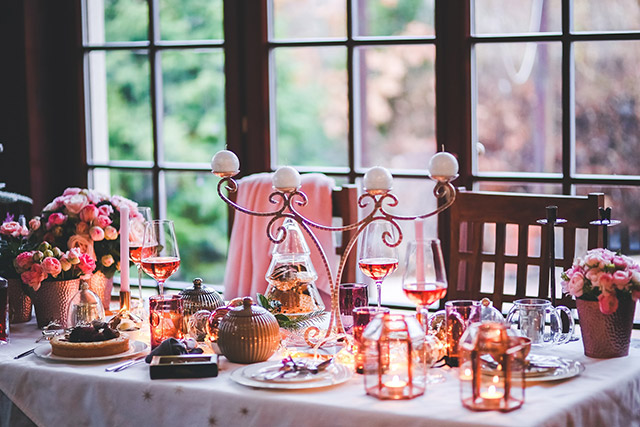 Mesa decorada en tonos rosa. Candelabro en oro rosa al centro de la mesa con velas tipo bola, porta velas de vidrio con estructura metálica color oro rosa, mantel y menaje blancos. Pequeños maceteros con rosas en algunos puntos de la mesa.