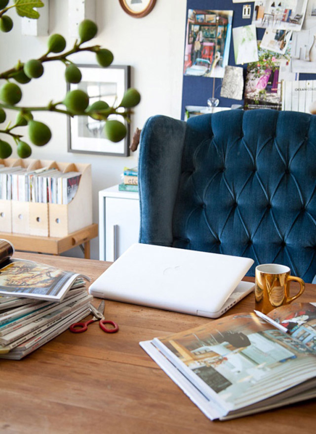 Detalle de mesa de escritorio con revistas, laptop y un tazón dorado.