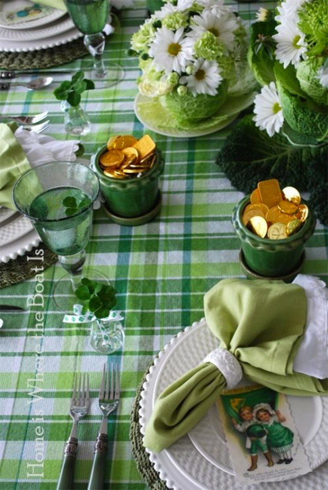 Mesa puesta a la irlandesa, con mantel a cuadros blanco y verde, copas de vidrio verde servidas con una hoja de trébol dentro y cada plato con una ilustración de una pareja irlandesa.